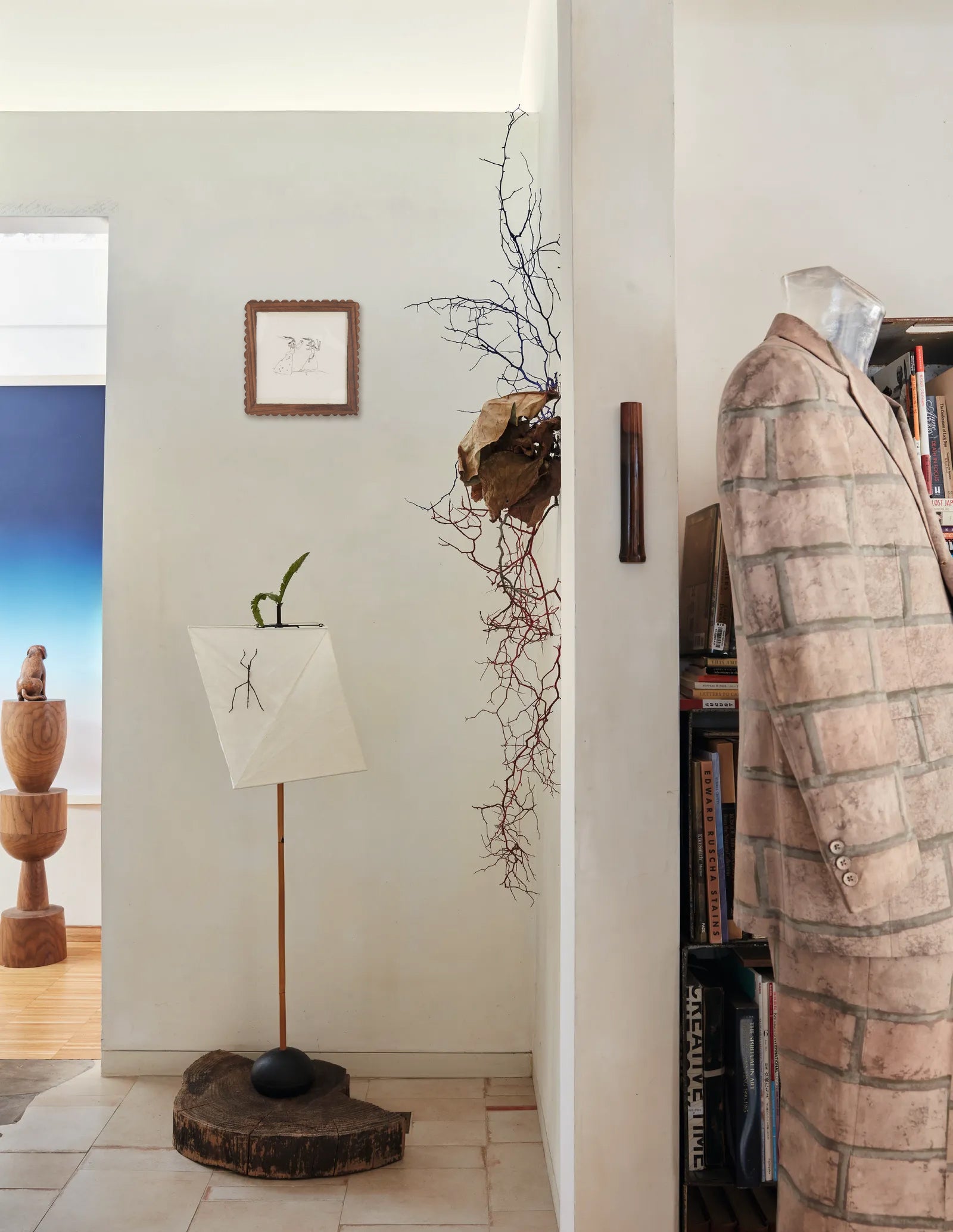 Room interior with a standing lamp, art in wooden frame, decorative plant, and coat on a rack.