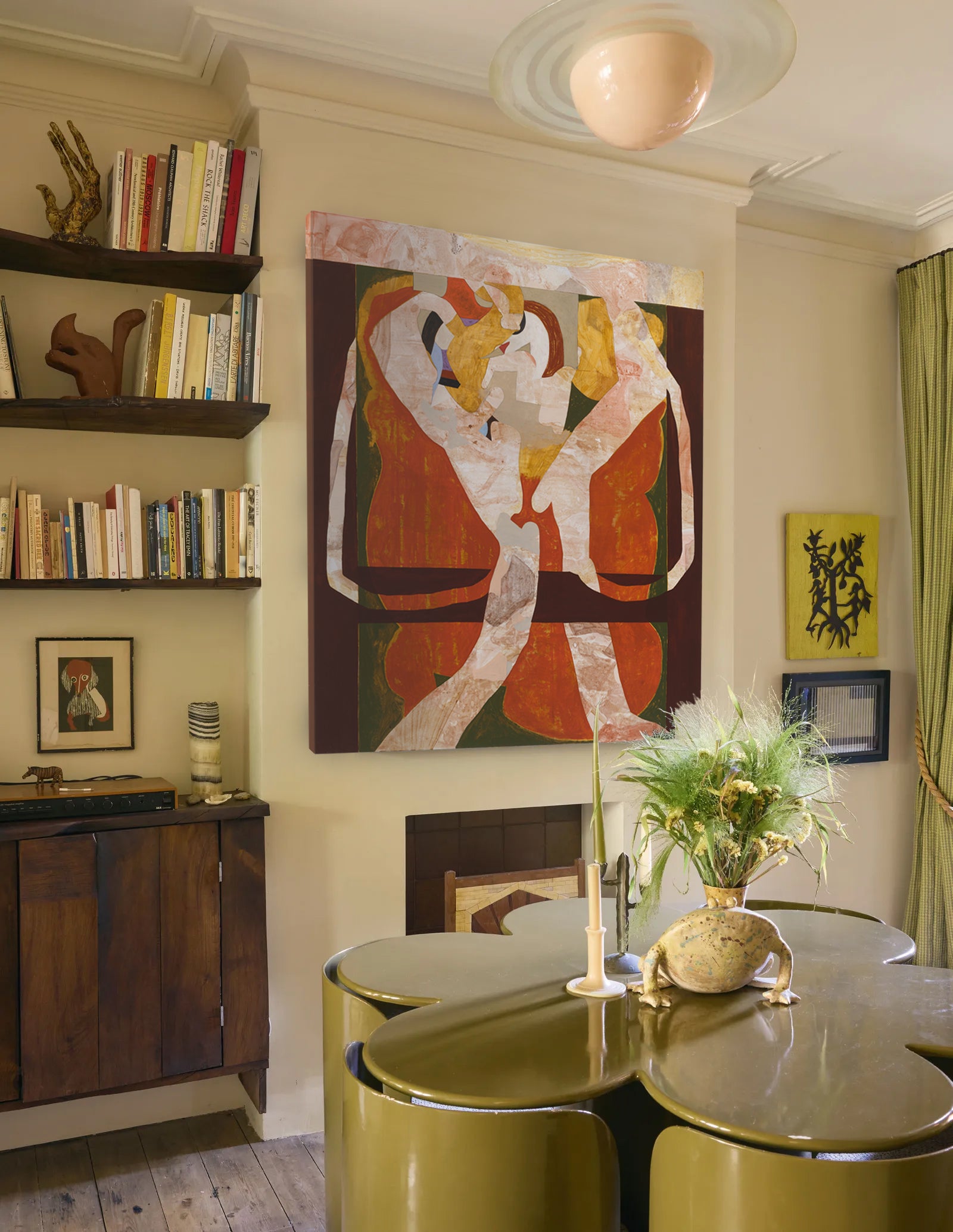 Dining room with a large abstract painting on the wall, green chairs, and a vase with flowers.