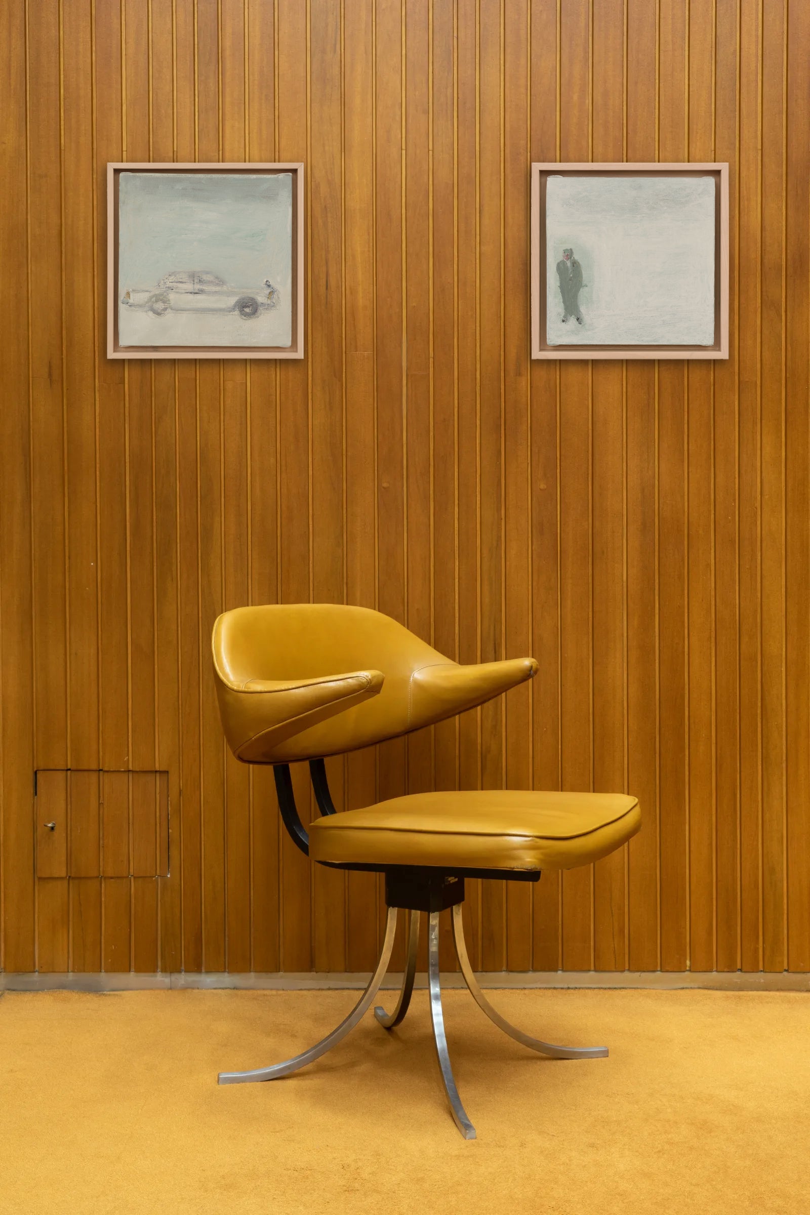 Yellow chair with a unique design against a wooden paneled wall with framed pictures.