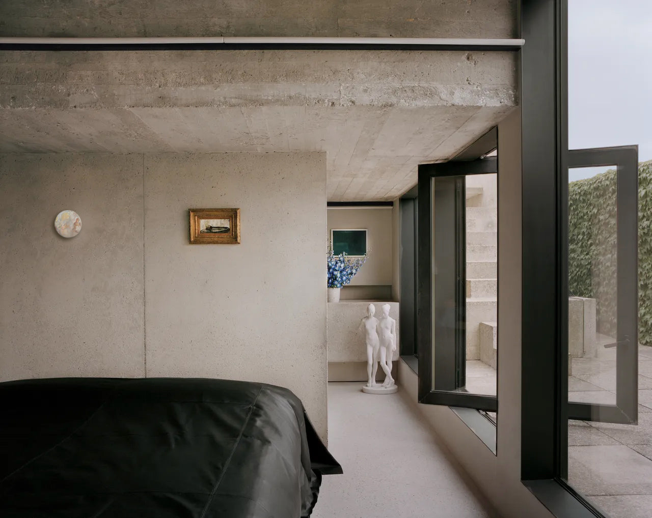 Modern bedroom with concrete ceiling and large windows overlooking a garden.