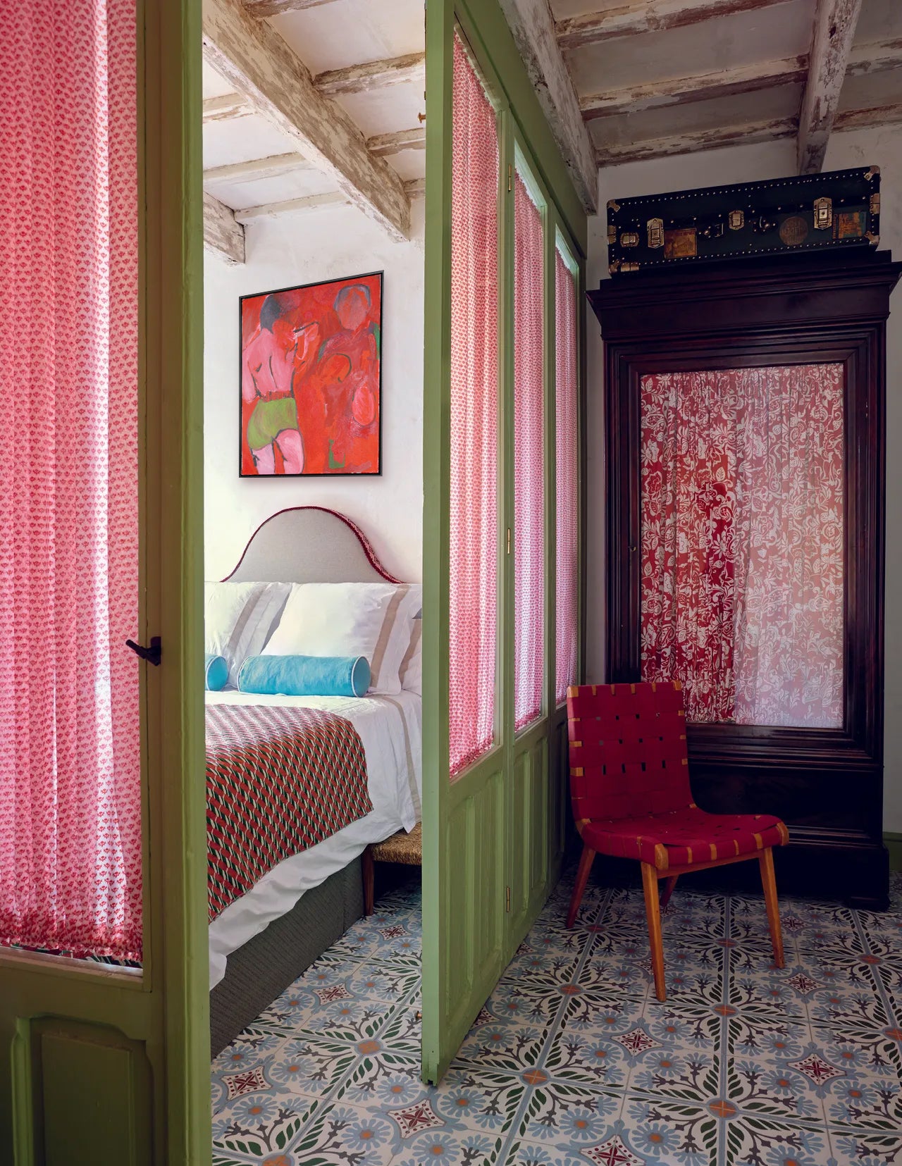 Room with pink curtains, floral bedspread, fine art and red chair.