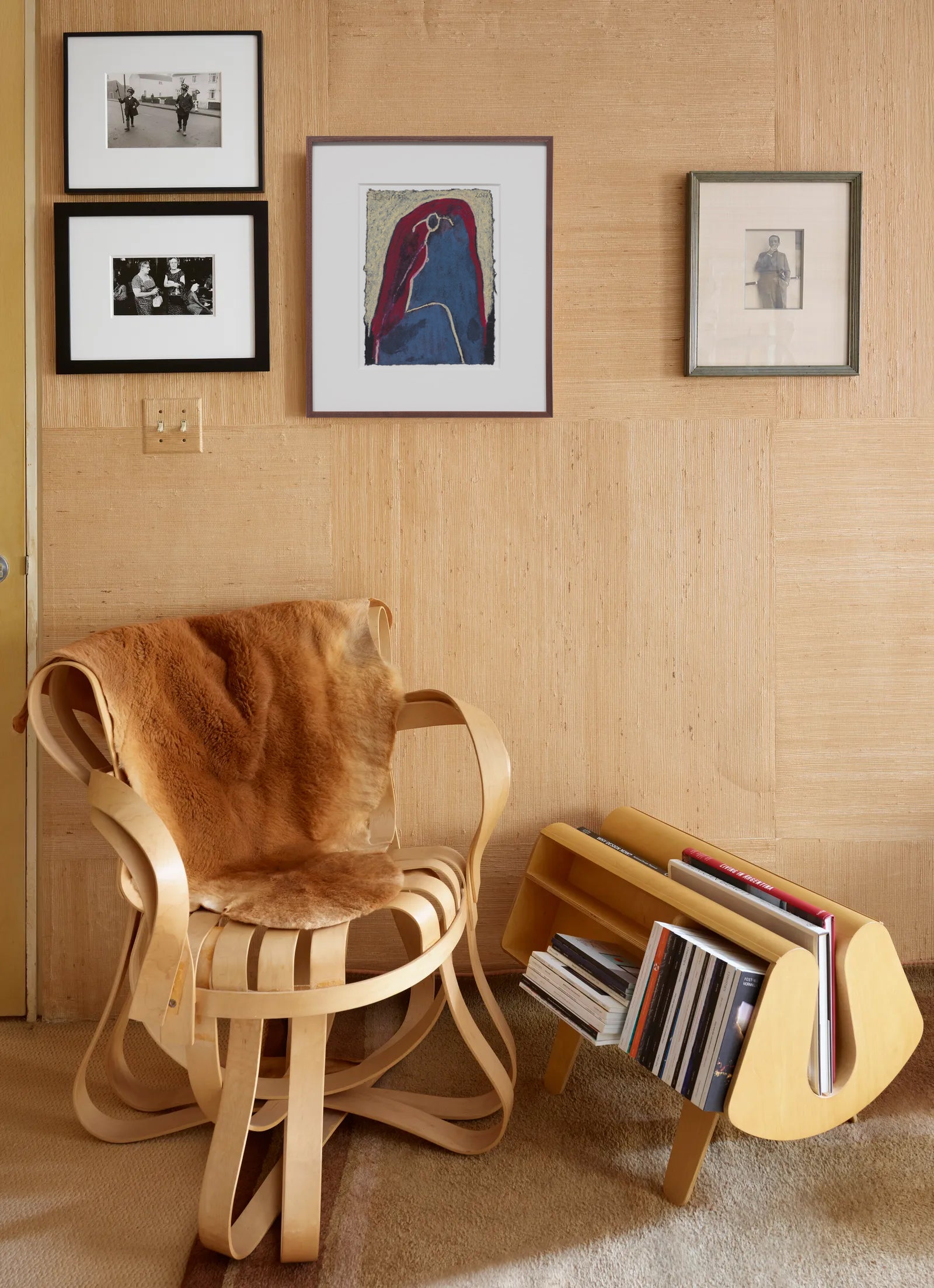 Wooden chair with a brown cushion and a wooden shelf with books against a wooden wall. Wall art and photographs.