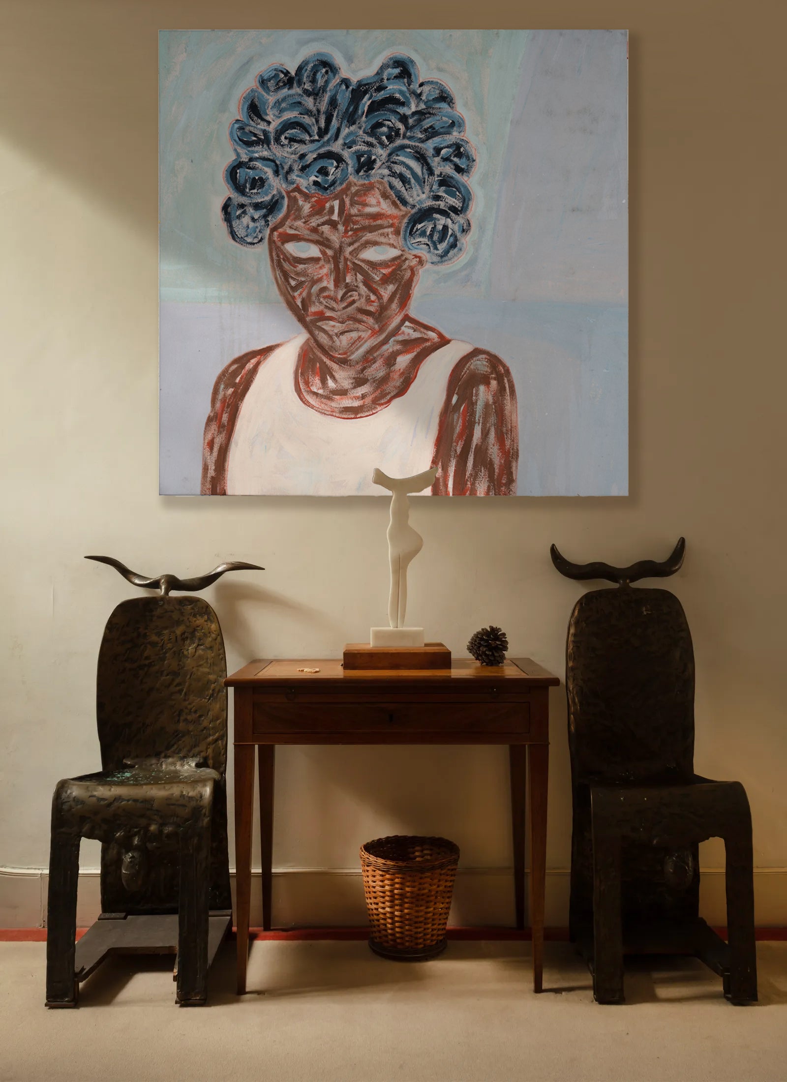 Room interior with a painting of a woman's face, two chairs, and a small table.