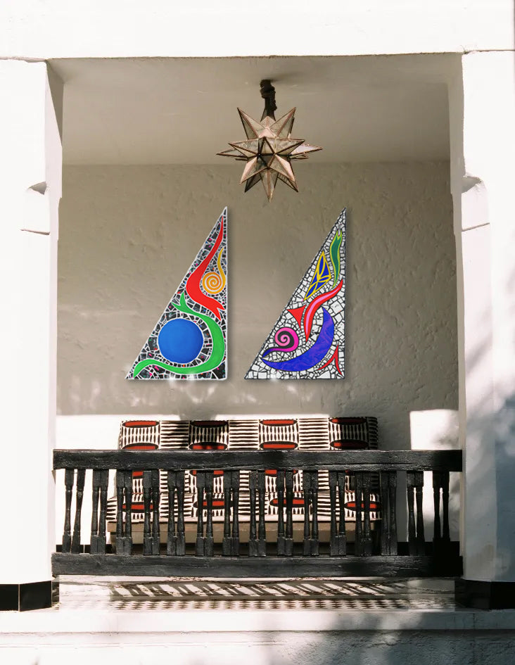 Two colorful triangular wall hangings on a gray wall above a wooden shelf with books.