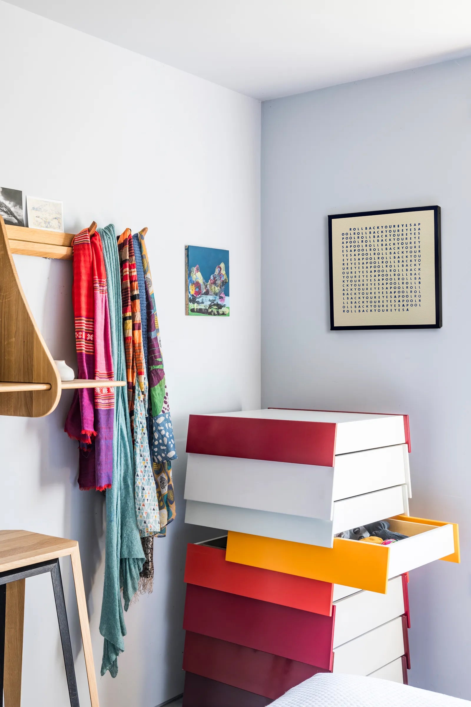 Colorful dresser with open drawer in a room with a shelf and wall art.